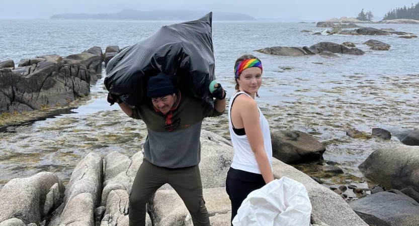 Two students pick up trash on a beach as part of a service project. 